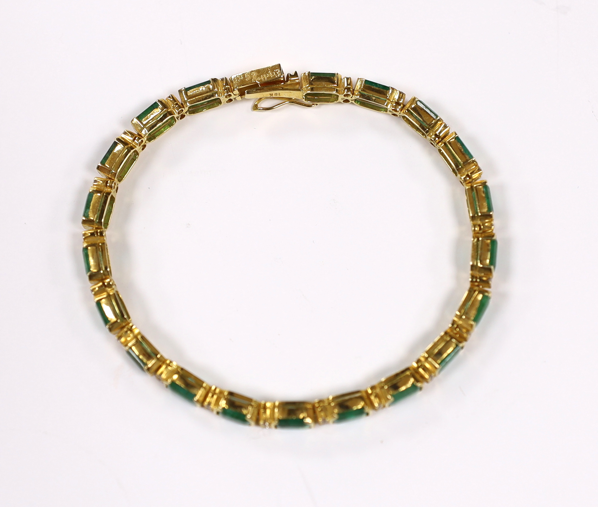 A modern 18k yellow metal and twenty stone emerald set line bracelet, with diamond chip spacers, 18cm, gross weight 13.5 grams.